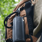 Black outdoor speaker hanging from a brown backpack.